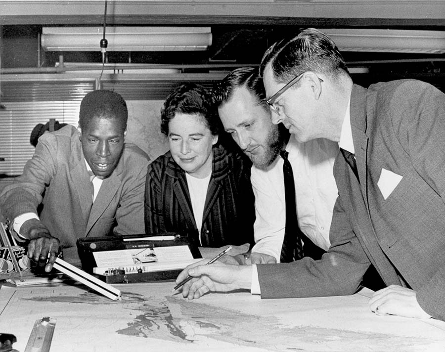 Four people looking over a map in 1960. Samuel Gaskin, an African Nova Scotian employee of the mapping department is on the left, pointing to a map with a ruler.