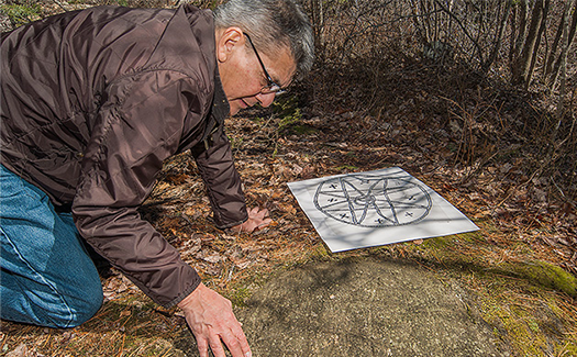 Roger Lewis, Curator of Mi’kmaq Cultural Heritage in the field examining a petroglyph.