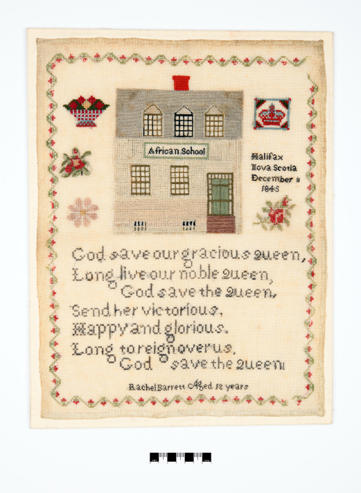 An unframed antique needlework sampler stitched on light-colored linen fabric, set against a plain white background. A green and red floral vine border encloses the entire design. The upper half features a detailed, cross-stitched rendering of a two-story building with a red chimney, labeled with the words "African School" across the front. Smaller stitched motifs flank the schoolhouse, including a flower basket, a crown inside a square, floral sprigs.