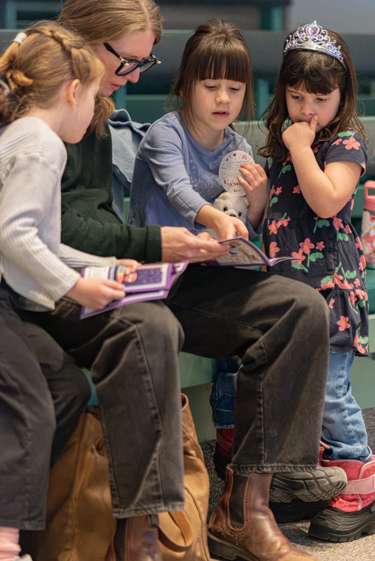 A woman reads to 3 girls in the Mighty Engine exhibit.