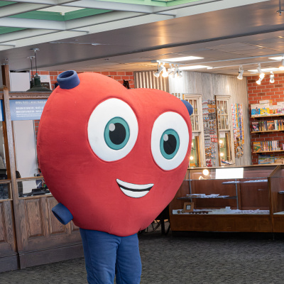 Heart mascot standing in the Museum of Industry lobby wearing blue pants and teal shoes