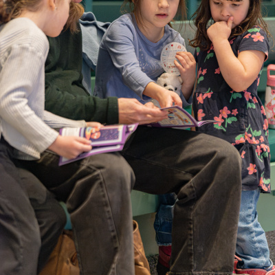 A woman reads to 3 girls in the Mighty Engine exhibit.