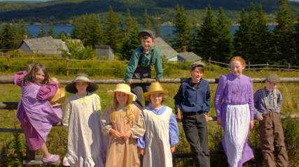 A group of children wearing costumes standing against a fence.