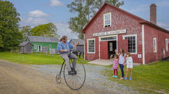 Visitors wave at a costumed interpreter on a penny-farthing 