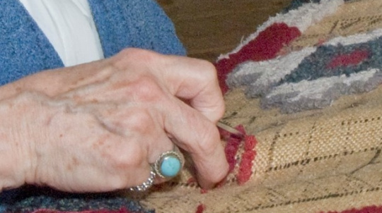 A close up of hands rug hooking