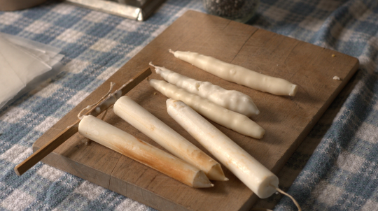 Hand made candles on a wooden board on a table.