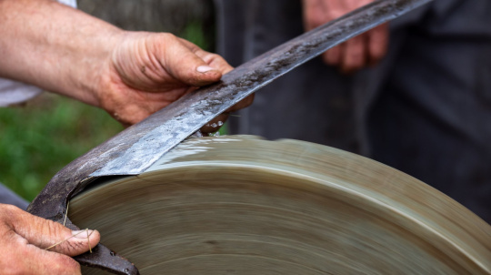 Hands sharpening a blade on a stone wheel.