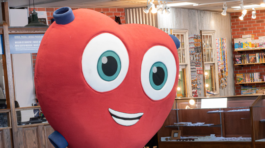 Heart mascot standing in the Museum of Industry lobby wearing blue pants and teal shoes