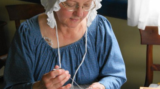 Costumed interpreter, a woman tatting at a table.