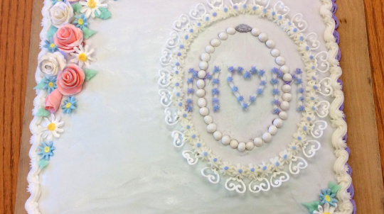 A square cake with flora decorations and the word MOM.