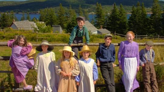 A group of children wearing costumes standing against a fence.