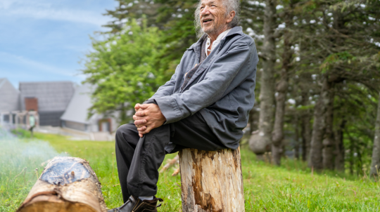 Man sitting on a stump in front of a log.