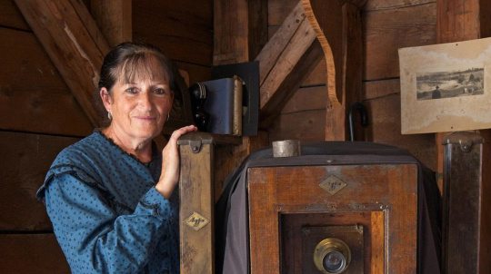 Costumed interpreter, leaning on an Ambrotype camera